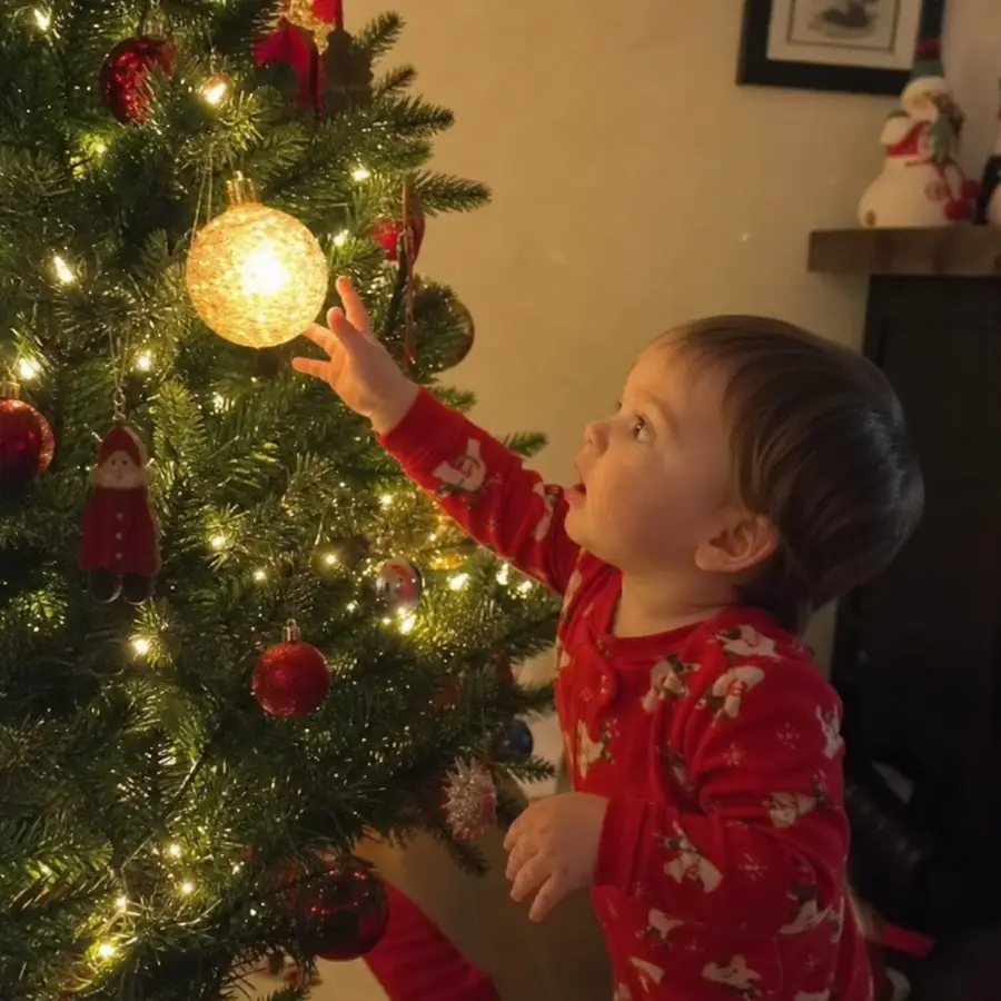 Toddler in red pajamas reaching for a glowing ornament on the Christmas tree