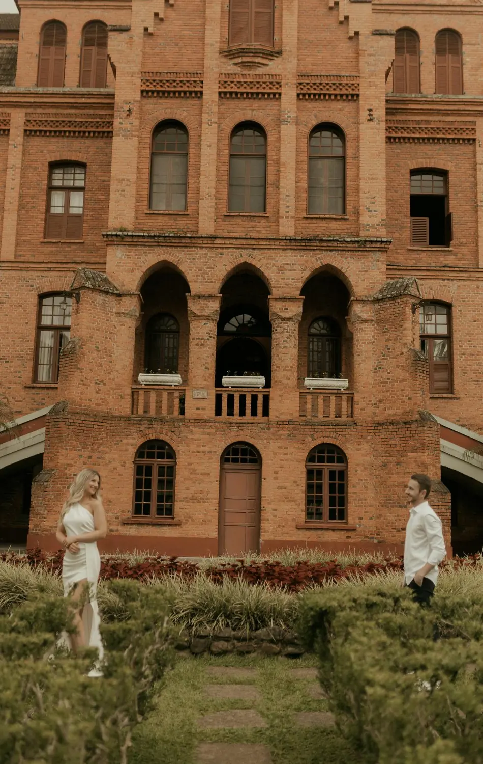 Two people in the garden of a historic red brick campus building