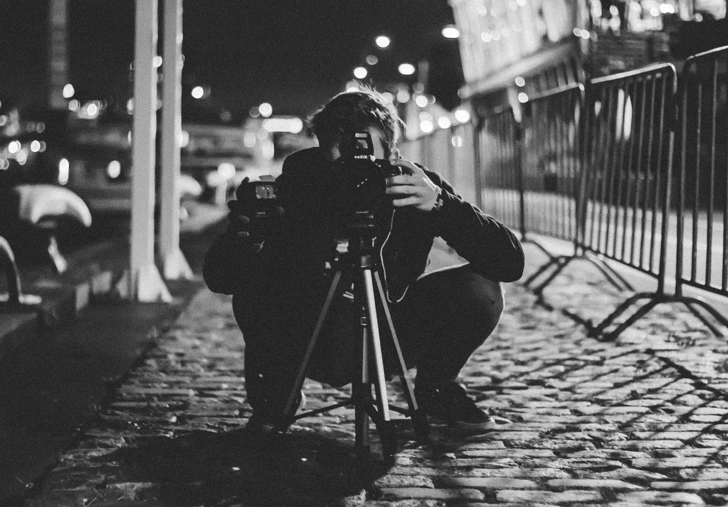 Photographer crouching behind a tripod on a street at night